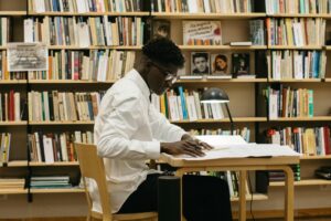 A determined student studying at a desk in a library full of bookshelves.